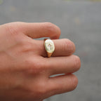 Hand wearing a gold ring with a diamond on a blurred background
