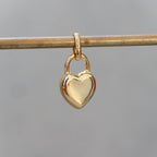 Gold heart-shaped lock pendant on a thin rod against a blurred background