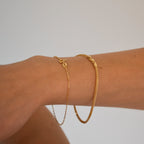 Gold bracelet on a wrist against a plain background